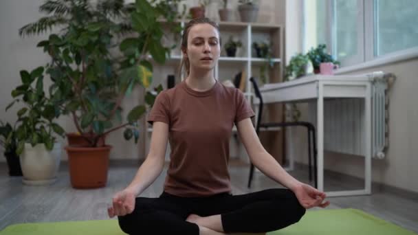 Blijf thuis, blijf fit. Mooie kalme jonge vrouw mediteren, doen yoga oefeningen terwijl zitten in lotus poseren op de vloer thuis — Stockvideo