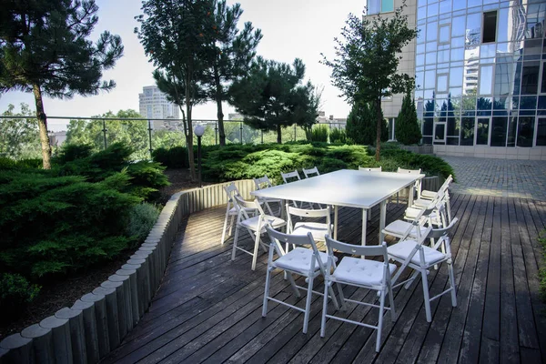 Parkta tahtada sandalyeler olan beyaz bir masa.