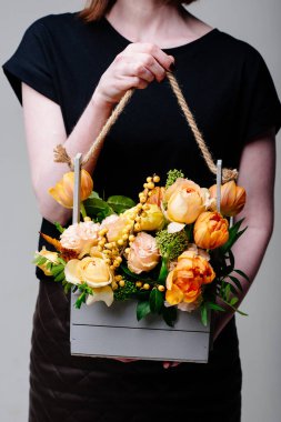Çiçekçi bir kadının elinde, tahta bir kutuda bir buket çiçek. Rosa spreyi Catalina, ilex, skimmia, karanfil, östoma, lale