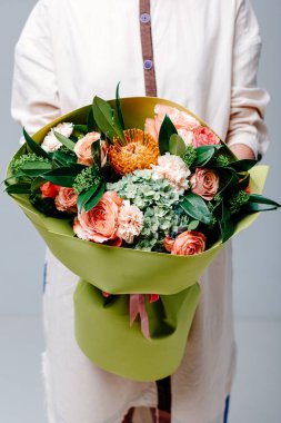 Çiçek buketi limon renginde foamiran paketi bir çiçekçinin elinde. Gül, ortanca, protea, yağsız.