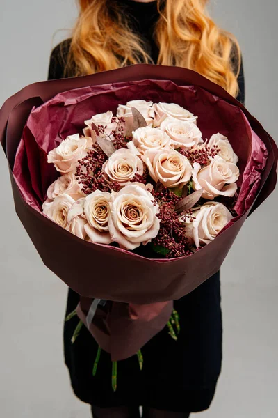 Kırmızı saçlı çiçekçi kızın elinde, açık arkaplandaki kırmızı çiçekli çiçek demeti. Gül Menta, okaliptüs.