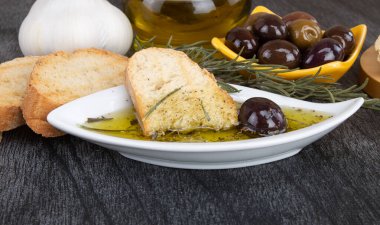 Zeytinyağına batırılmış zeytinyağlı ekmek. Yunan zeytinyağlı ekmek sosu. Baharatlı ve otlu yağlı İtalyan ekmeği. Beyaz kasede zeytinyağı sosu ve ahşap zemin üzerinde Yunan zeytinleri. 