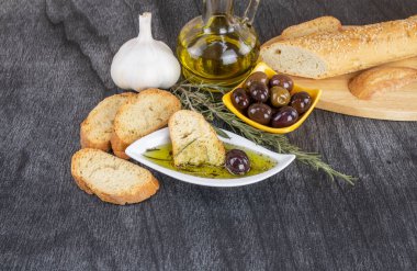 Zeytinyağına batırılmış zeytinyağlı ekmek. Yunan zeytinyağlı ekmek sosu. Beyaz kasede zeytinyağı sosu ve ahşap zemin üzerinde Yunan zeytinleri. Uzayı metin için kopyala. Ekmek batırma konsepti Akdeniz yemekleri.