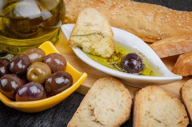 Zeytinyağına batırılmış zeytinyağlı ekmek. Yunan zeytinyağlı ekmek sosu. Baharatlı ve otlu yağlı İtalyan ekmeği. Beyaz kasede zeytinyağı sosu ve ahşap zemin üzerinde Yunan zeytinleri. 