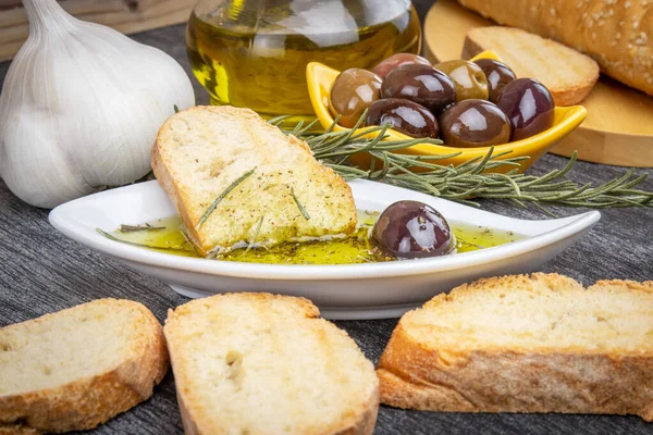 Greek olive oil bread dip. Bread with Oil for Dipping with Herbs & Spices. Close up Olive oil sauce in white bowl & Greek olives on wood background.