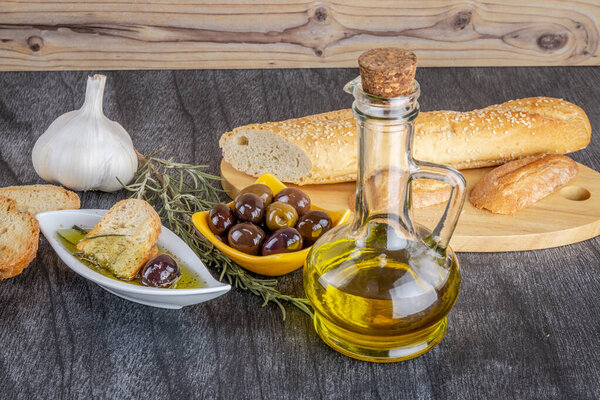 Bread dip, olive oil, garlic olive and rosemary on grey wooden table. Copy space for text. Natural delicatese food. Greek olive oil sauce.
