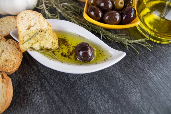 The bread dipped in olive oil with olive. Greek olive oil bread dip. Italian Bread with Oil for Dipping with Herbs & Spices. Olive oil sauce in white bowl & Greek olives on wood background.