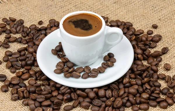 Cup of Greek coffee on sack background with coffee beans. Turkish coffee in white small mug. Traditional Greek coffee concept.