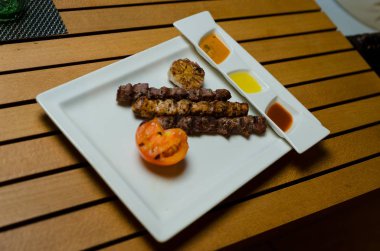 Beyaz plaka üzerinde servis kurulu, baharatlı domates sosu, otlar, Beyaz ahşap zemin üzerinde ızgara kuzu şiş kebap.
