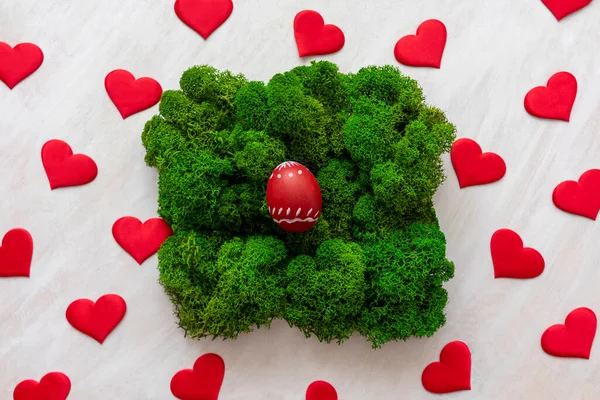 Red egg in moss and red hearts around. Easter festive concept wuth love.