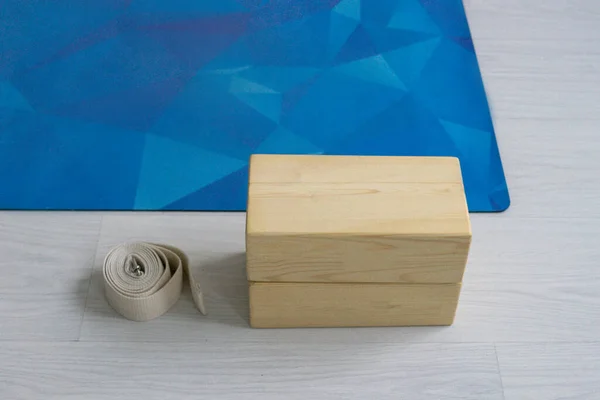 Composition from yoga props. Blue mat, blocks, and belt on light background.