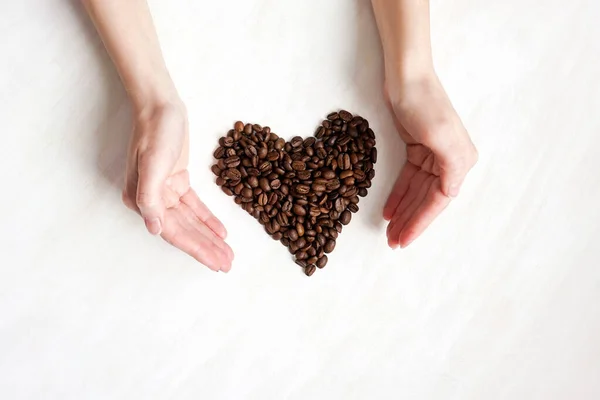 heart of cofee grains between hands on white wooden background