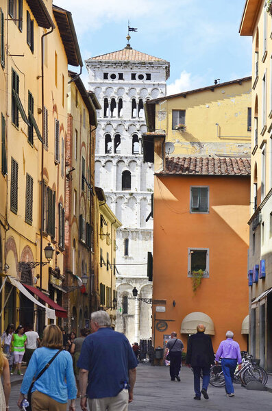 Lucca, Italy - June 11th 2012: Unidentified people in narrow street with bell tower in background
