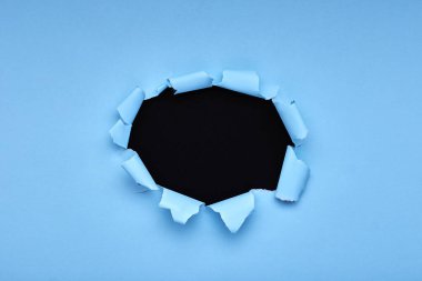 Mavi kağıtta bir delik. Yırtılmış. Siyah ahşap arka plan. Soyut arkaplan