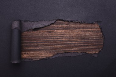 Siyah kağıtta bir delik. Yırtılmış. Ahşap arka plan. Soyut arkaplan.