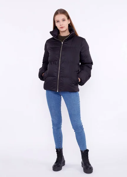 Young girl in a black down jacket and blue jeans isolated on a white background. — Stock Photo, Image