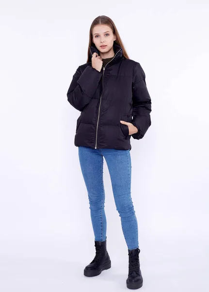 Young girl in a black down jacket and blue jeans isolated on a white background. — Stock Photo, Image