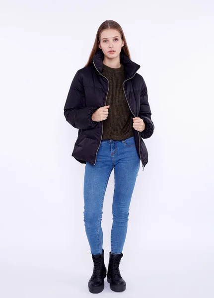 Ung flicka i svart dunjacka och blå jeans isolerad på en vit bakgrund. — Stockfoto