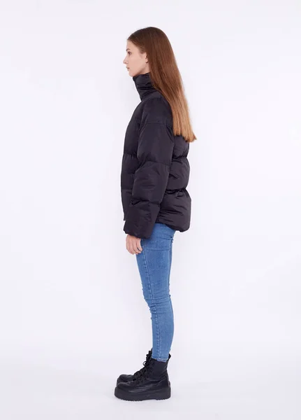 Ung flicka i svart dunjacka och blå jeans isolerad på en vit bakgrund. — Stockfoto