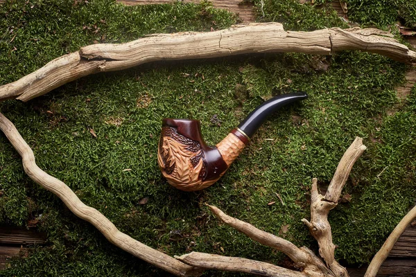 Tobacco pipe on green moss background.