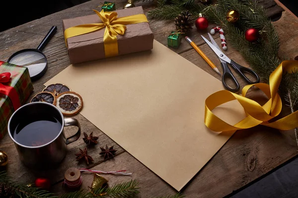 A wish list. Old paper sheet with pencil at grunge wooden background with copy space. Christmas tree, gift, cones, dried citrus fruits, magnifying glass, cinnamon, scissors. Cup of tea.