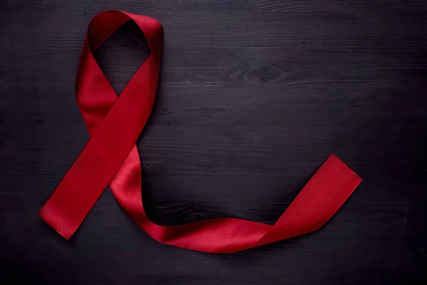 Doença da SIDA. Fita vermelha em fundo de madeira preta, vista superior, espaço de cópia . — Fotografia de Stock