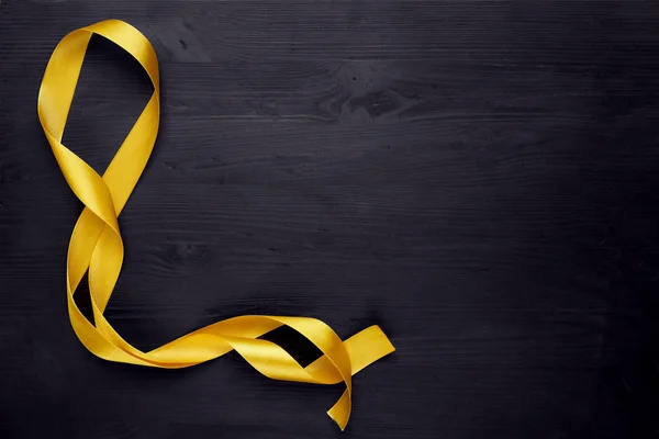 Golden, yellow ribbon bow on black wooden background. Copy space.