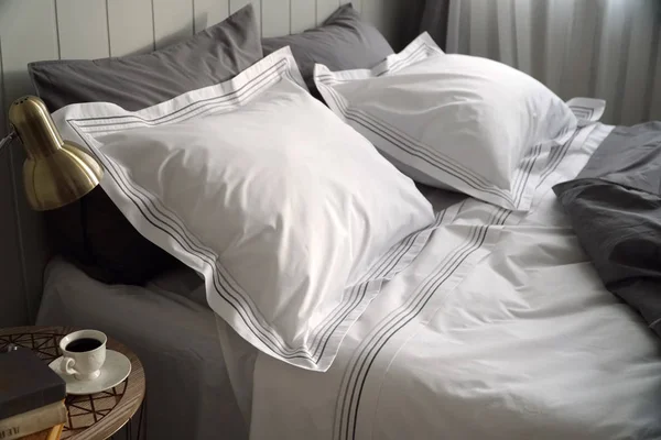 Cuscini bianchi e grigi e coperta su letto bianco in spaziosa camera da letto interna . — Foto Stock