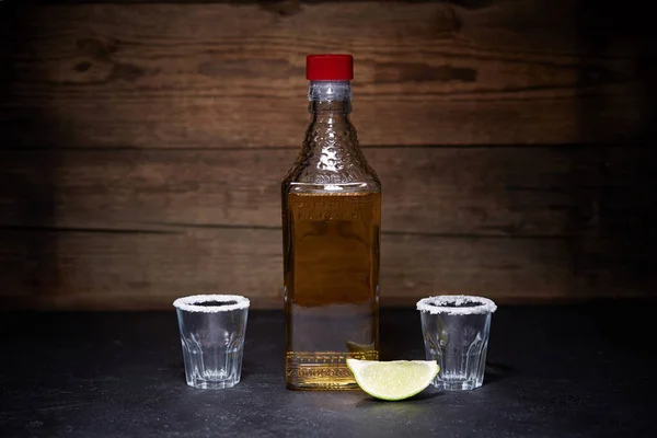 Arany tequila felvételek lime gyümölcsök fa háttér. Egy üveg tequila.. — Stock Fotó