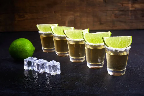 Mexikanska tequila guld i korta glas med salt, lime skivor och is på ett träbord. Rök. — Stockfoto