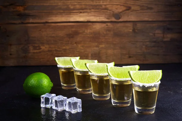 Mexican tequila gold in short glasses with salt, lime slices and ice on a wooden table. Smoke.