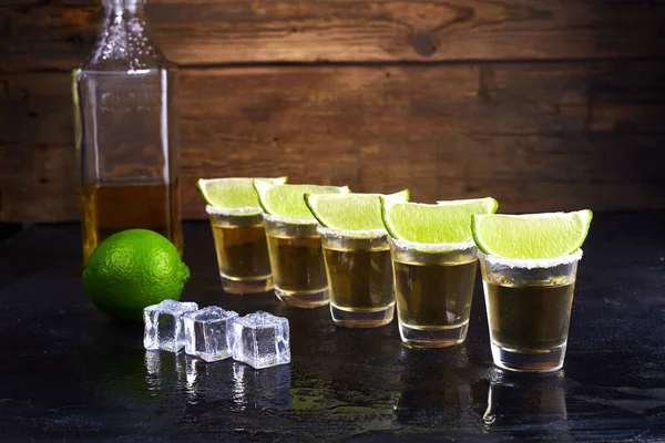 Ouro de tequila mexicano em copos curtos com sal, fatias de limão e gelo em uma mesa de madeira. Fumar . — Fotografia de Stock