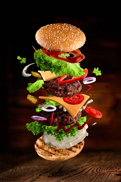 Maxi hamburger, dvojitý cheeseburger s létajícími ingrediencemi izolovanými na dřevěném pozadí. Obrázek ve vysokém rozlišení — Stock fotografie