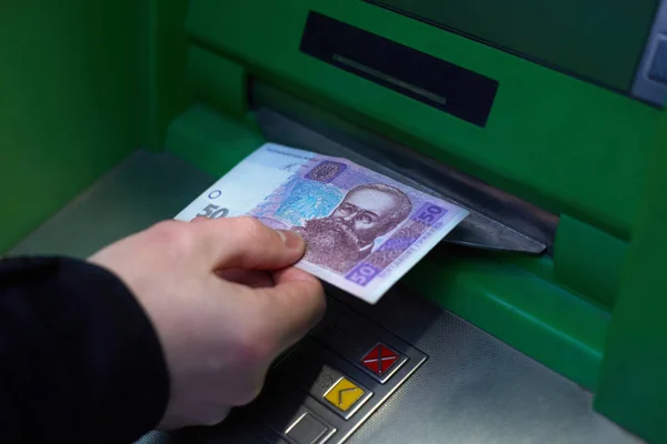 Männliche Hand, während sie 50 ukrainische Griwna von einem Geldautomaten abhob. die Abwertung der Landeswährung Griwna. — Stockfoto