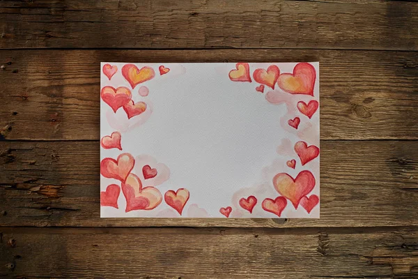 Aquarellpapier mit bemalten roten Herzen auf einem hölzernen Hintergrund. Kopierraum. — Stockfoto