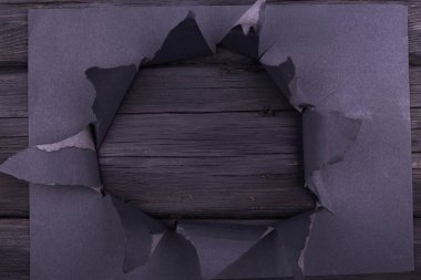 Siyah kağıtta büyük bir delik var. Yırtılmış. Siyah ahşap arka plan. Soyut arkaplan.