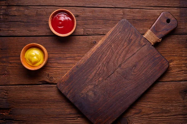 深色木制切菜板和酱汁在黑暗厨房桌子上 顶部视图 — 图库照片
