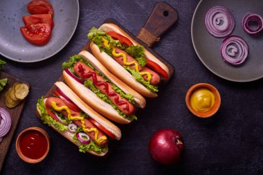 Sosisli, kızarmış soğan, kişniş yaprağı, peynir sosu ve hardallı sosisli sandviç, siyah beton dokunun üzerinde servis ediliyor. Fast food. Üst görünüm, alanı kopyala