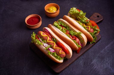 Sosisli, kızarmış soğan, kişniş yaprağı, peynir sosu ve hardallı sosisli sandviç, siyah beton dokunun üzerinde servis ediliyor. Fast food. Üst görünüm, alanı kopyala