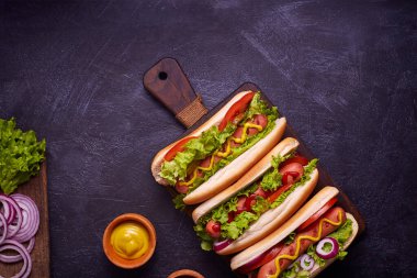 Sosisli, kızarmış soğan, kişniş yaprağı, peynir sosu ve hardallı sosisli sandviç, siyah beton dokunun üzerinde servis ediliyor. Fast food. Üst görünüm, alanı kopyala