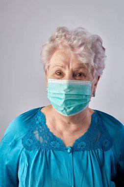 Yaşlı kadın koronavirüs yardımcısı. Yaşlı kadın evde tecrit edilmiş. Ev aktiviteleri. Evde kal. Büyükannem karantina sırasında yüz koruma maskeleri dikiyor. Koruyucu maske takan yaşlı kadın. COVID-19 kavramı.
