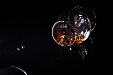 Konyaklı keskin nişancı bardağı (brendi bardağı, konyak kasesi, konyak bardağı veya balon) siyah arka planda yansıma ile yatar..