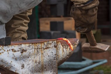 Bir demirci elinde çekiçle örse sıcak metalden bir ürün hazırlar.