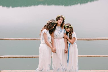 Anne ve iki kızı beyaz elbiseler kır çiçekleri çelenk ile göle yakın yürüyüş