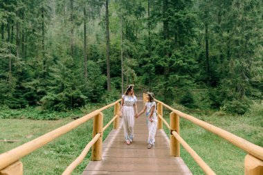 Anne ve iki kızı beyaz elbiseler kır çiçekleri çelenk ile göle yakın yürüyüş