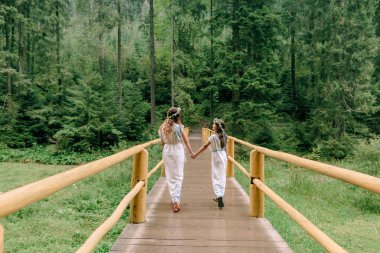 Anne ve iki kızı beyaz elbiseler kır çiçekleri çelenk ile göle yakın yürüyüş