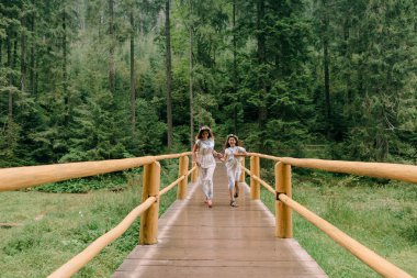 Anne ve iki kızı beyaz elbiseler kır çiçekleri çelenk ile göle yakın yürüyüş