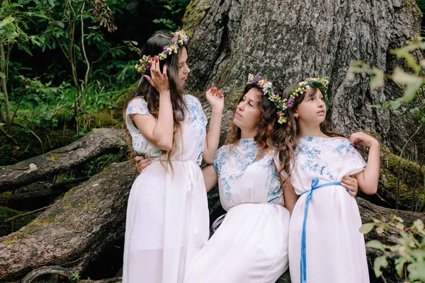 Mom and two daughters walking near the lake in white dresses with wreaths of wildflowers