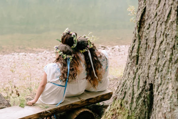 Mom and two daughters walking near the lake in white dresses with wreaths of wildflowers