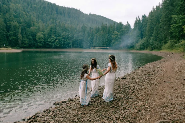 ママと 2 人の娘の野生の花の花輪と白いドレスの湖付近の散歩 — ストック写真